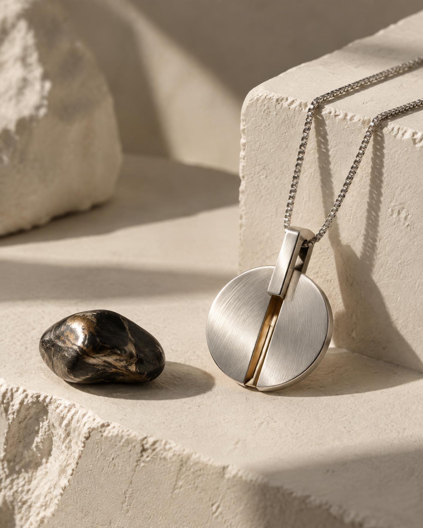 Minimal brushed silver pendant resting on warm mineral surfaces